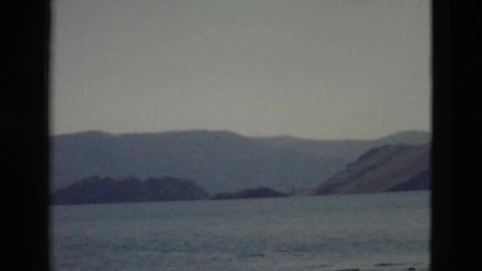A boat-level view across Yellowstone lake water toward low landforms and distant mountains in faded 8mm color.