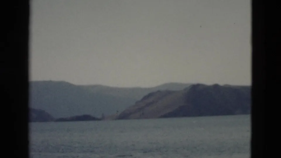 Vintage Yellowstone lake view from a moving boat, with broad water and muted hills framed by dark 8mm edges.