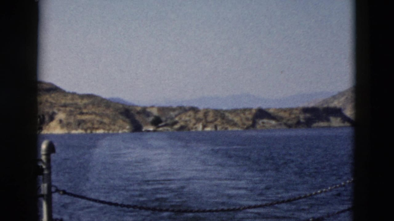 Rocky shoreline across blue water, framed by dark vertical window edges.