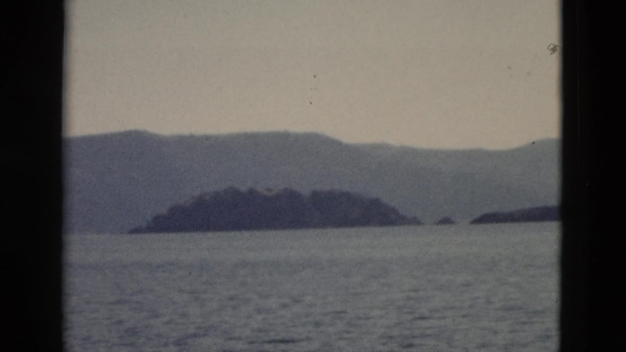 1958 Yellowstone-area lake view with distant island shapes, layered mountains, pale sky, and dark window framing.