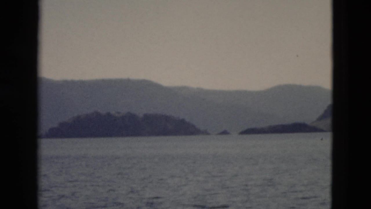 A 1958 Yellowstone lake scene shows island silhouettes and distant ridges through a dark window or boat frame.