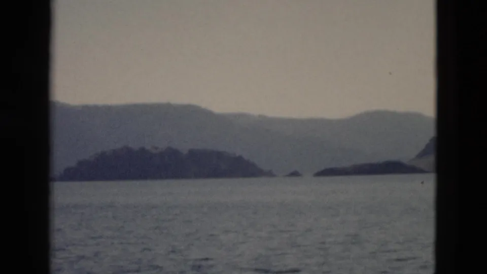 A 1958 Yellowstone lake scene shows island silhouettes and distant ridges through a dark window or boat frame.