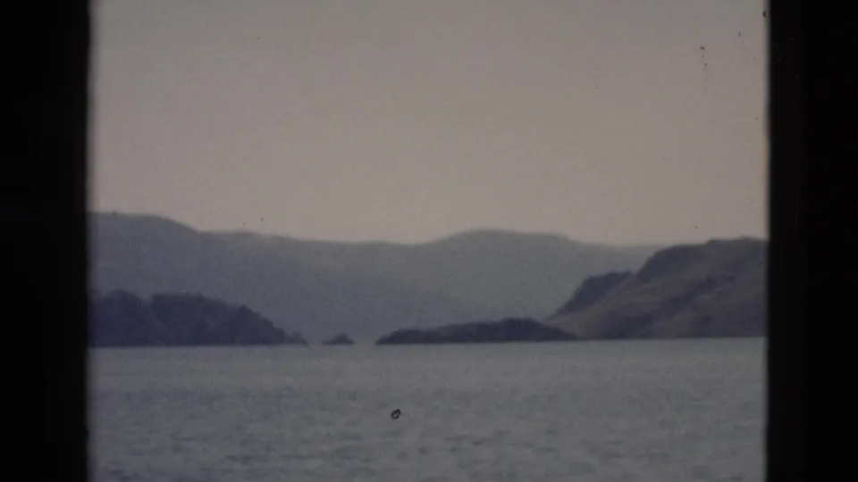 A 1958 Yellowstone water view shows low islands, a sloping mountain shoreline, and subdued sky through a dark divider.