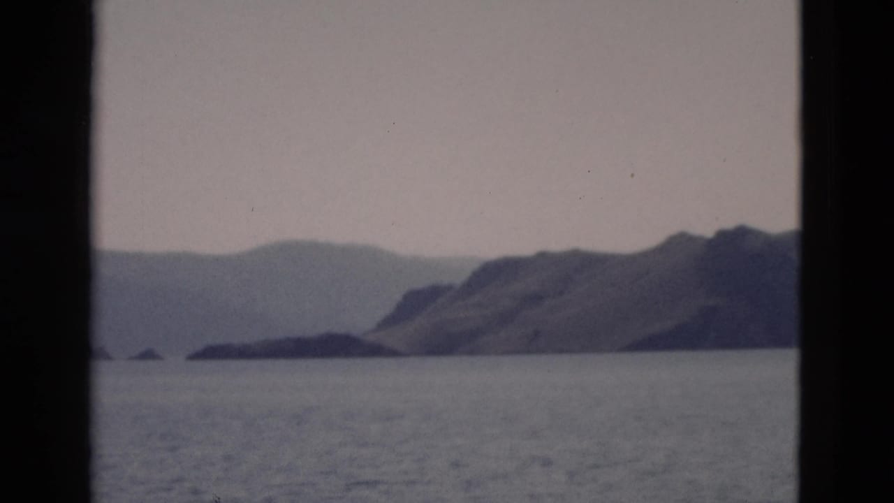 1958 Yellowstone-area water view showing a low shoreline, mountain ridge, muted sky, and dark vertical borders from the film frame or window.