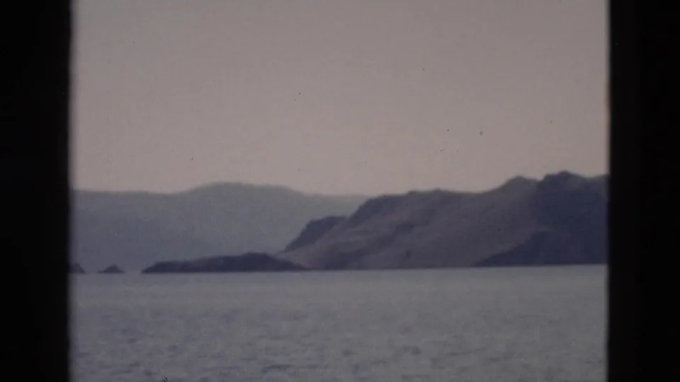 1958 Yellowstone-area water view showing a low shoreline, mountain ridge, muted sky, and dark vertical borders from the film frame or window.