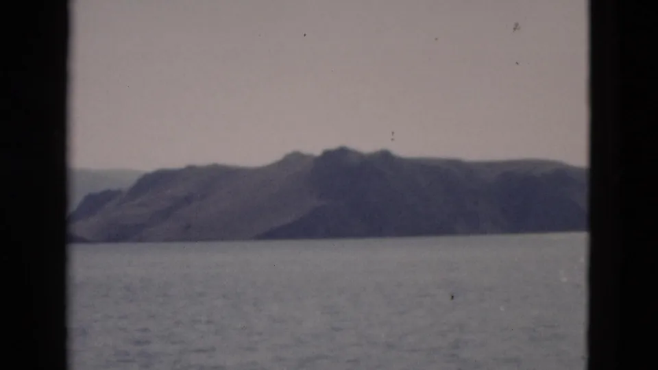 1958 Yellowstone-area lake scene with a broad mountain slope beyond the water, pale sky, soft focus, and visible film grain.