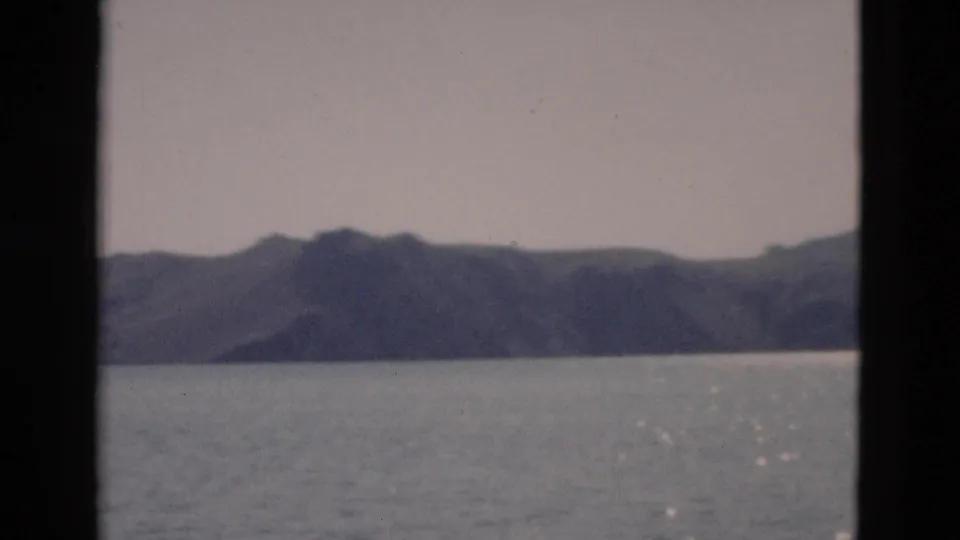 1958 Yellowstone-area lake view with a dark mountain range, calm water, muted sky, and small light glints near the lower right.