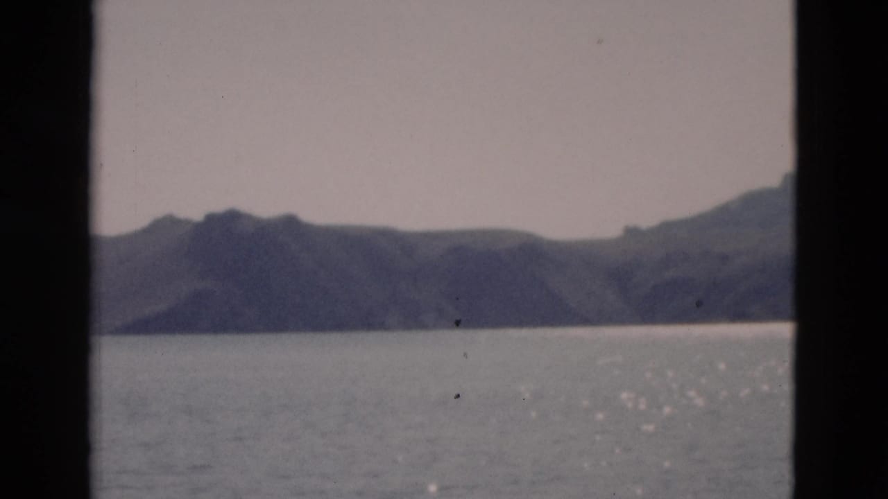 1958 Yellowstone home-movie frame showing a calm lake, distant mountains, pale sky, and visible 8mm frame borders.