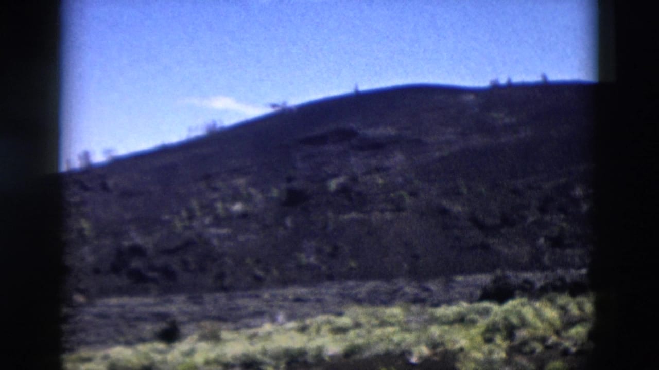 1958 Yellowstone view of a rolling rocky hill with scattered shrubs and a bright blue sky above.