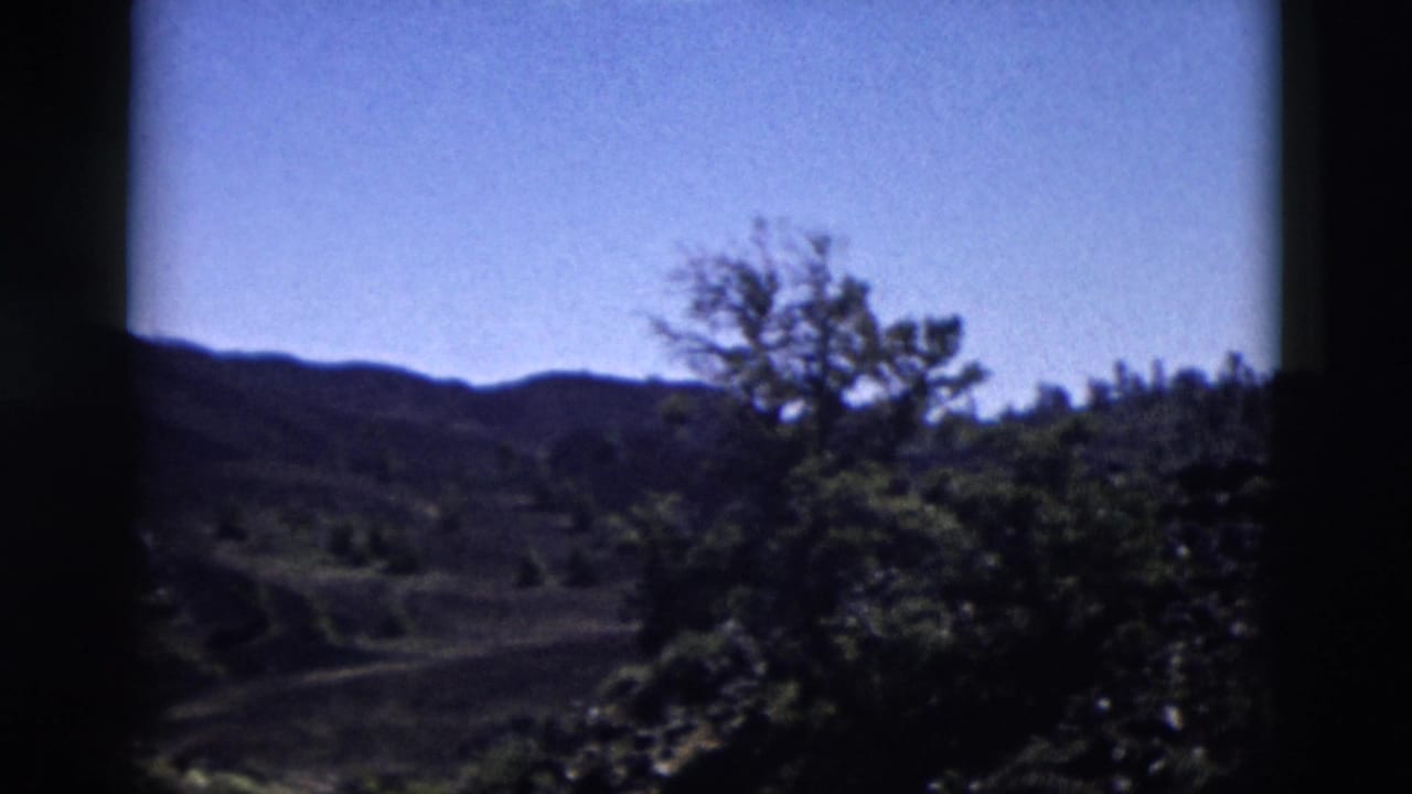 Dark volcanic landscape with shrubs, hills, blue sky, and heavy 8mm frame edges.