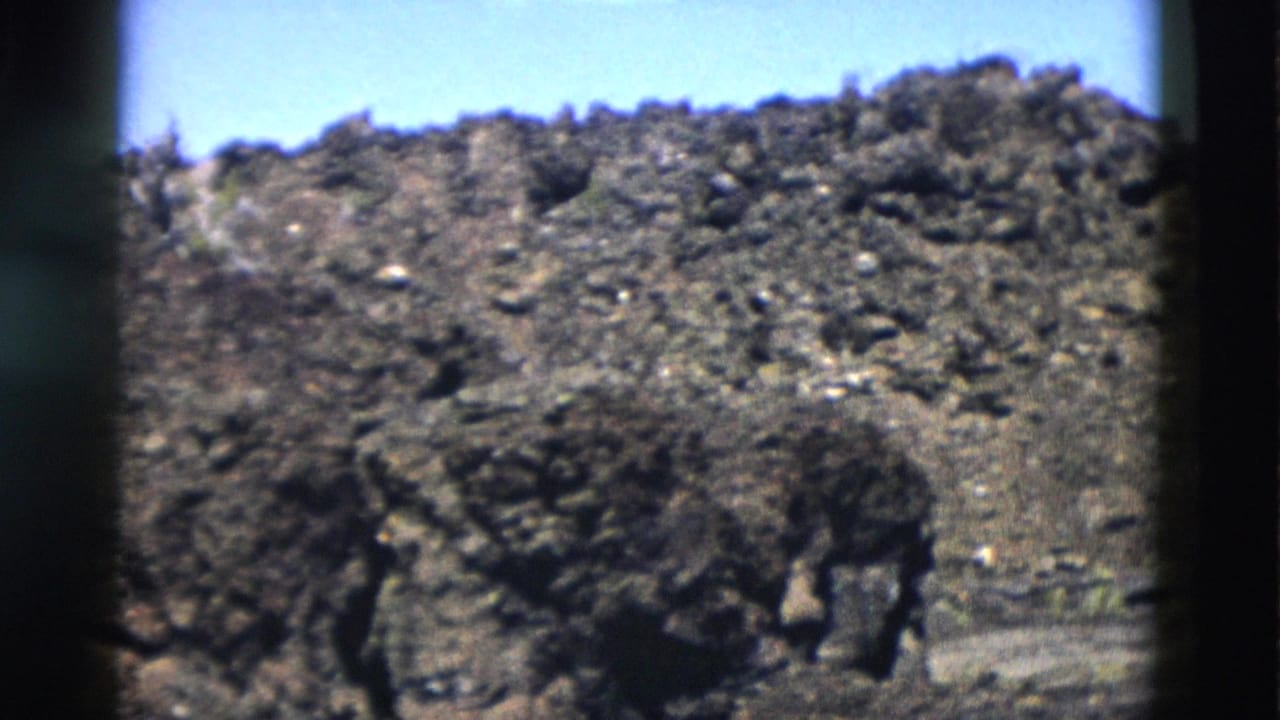 Yellowstone 8mm frame from 1958 showing a sunlit rocky rise with scattered scrub and a clear blue sky.