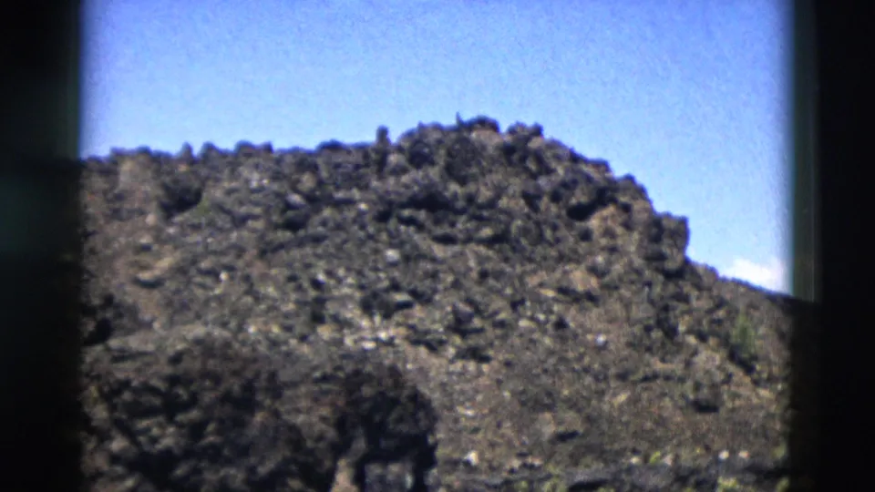 1958 Yellowstone home-movie frame showing a rocky mound, open sky, and scattered low vegetation near the base.