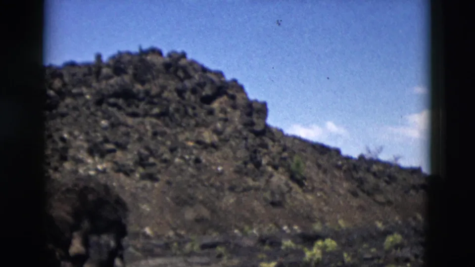 Yellowstone 1958 8mm frame showing a rocky ridge, blue sky, sparse scrub, and a dark foreground shape possibly near the camera.