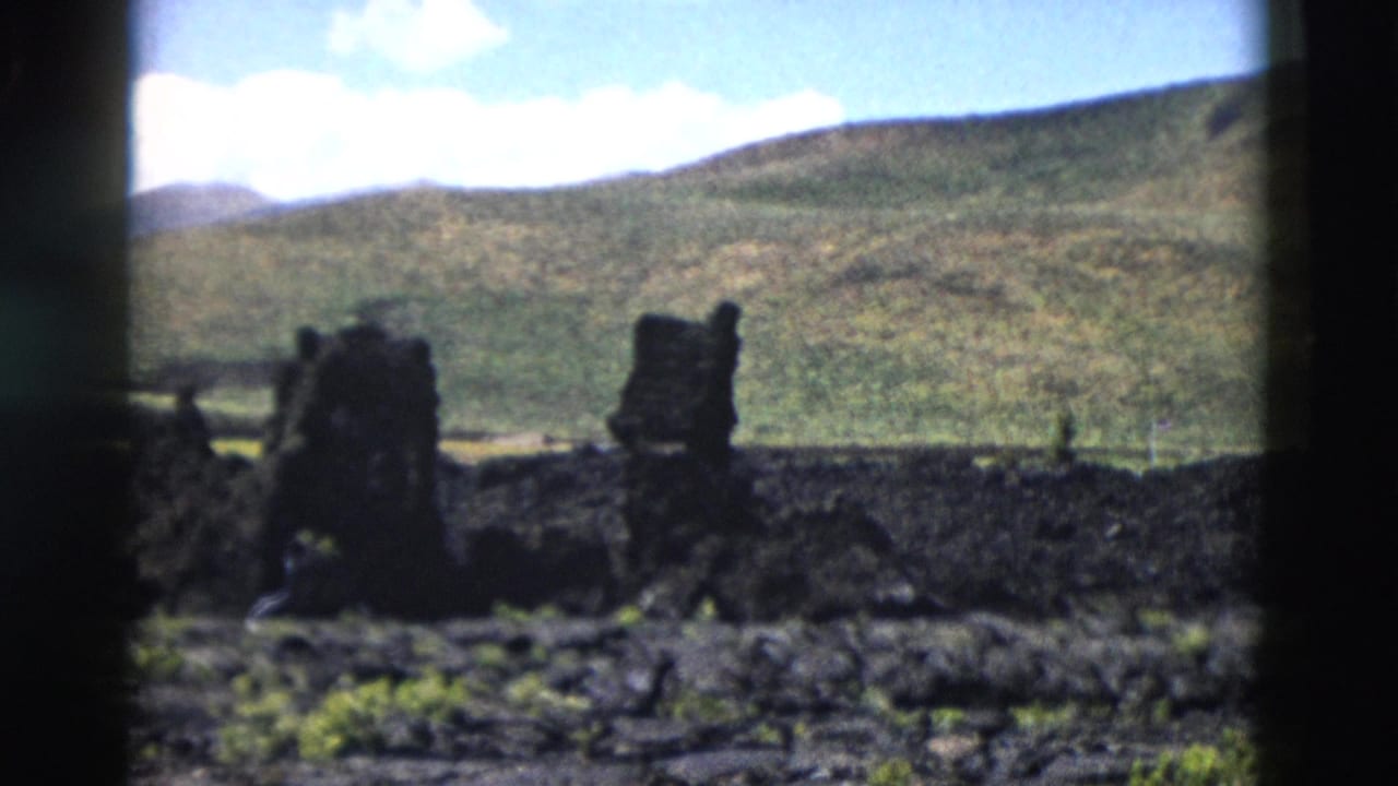 1958 Yellowstone frame with dark lava formations silhouetted against rolling green hills and bright clouds.