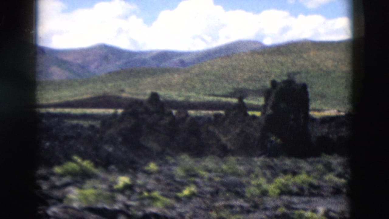 Yellowstone volcanic terrain appears in soft focus, with dark rock forms, low vegetation, hills, and bright clouds.