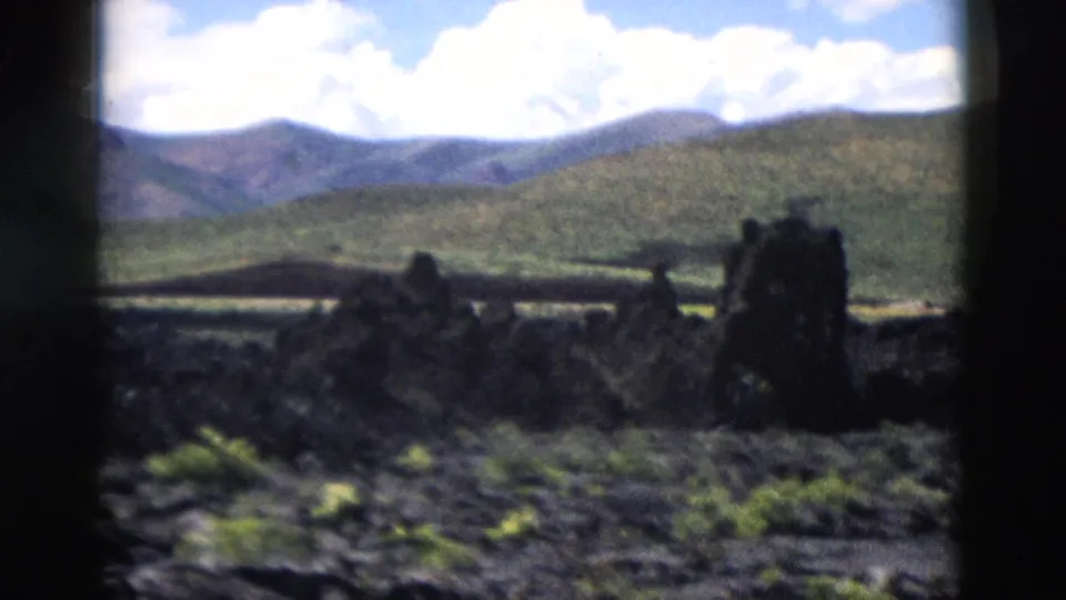 Yellowstone volcanic terrain appears in soft focus, with dark rock forms, low vegetation, hills, and bright clouds.