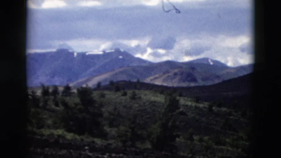 1958 Yellowstone home-movie view of distant snow-dusted mountains, cloudy sky, dark hills, and soft foreground shrubs.