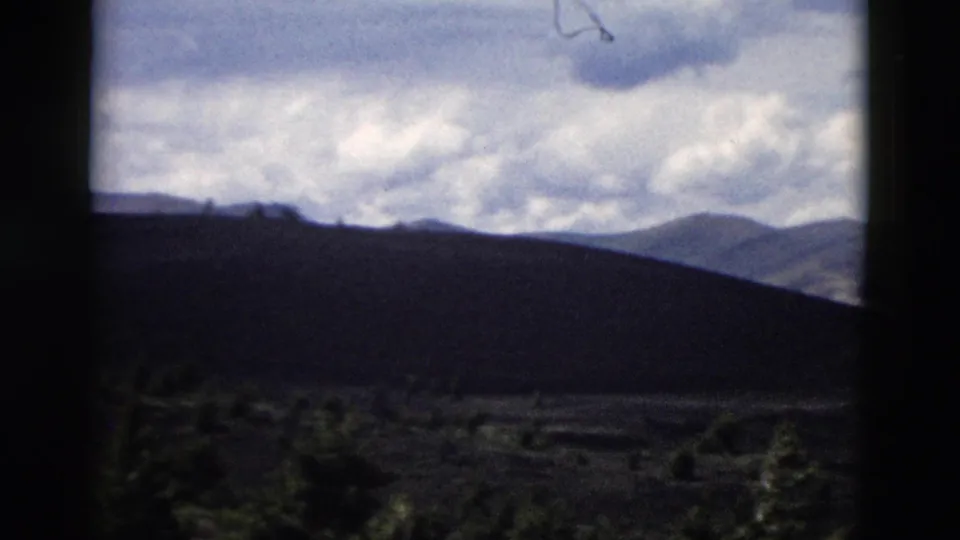 1958 Yellowstone frame with dark foreground hills, far mountain peaks, evergreen cover, and bright cloud layers.