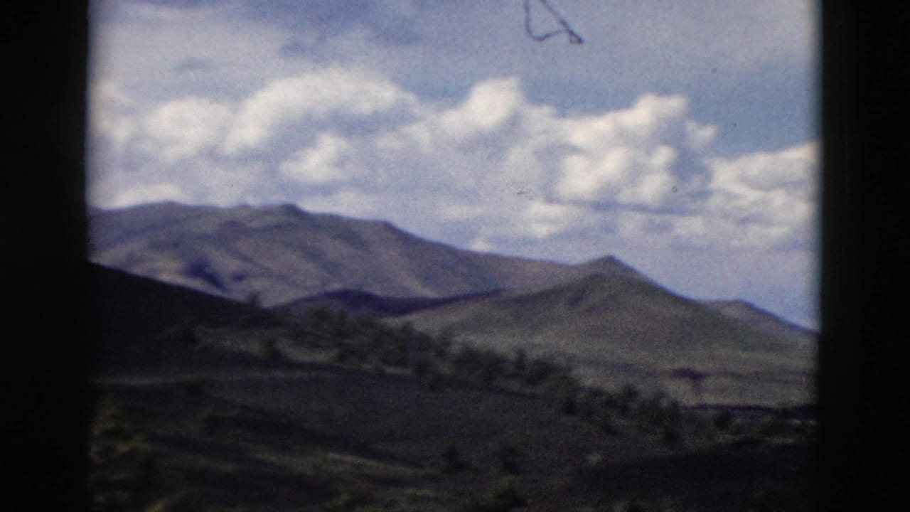 1958 Yellowstone-area 8mm view of rolling hills, distant ridges, sparse tree lines, and bright clouds.