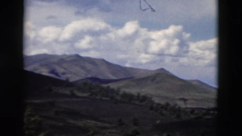 1958 Yellowstone-area 8mm view of rolling hills, distant ridges, sparse tree lines, and bright clouds.