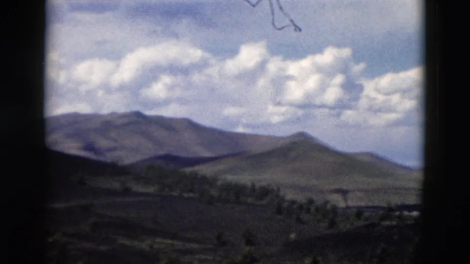 Yellowstone-area travel footage from 1958 showing a rounded hill, darker ridge line, valley trees, and high clouds.