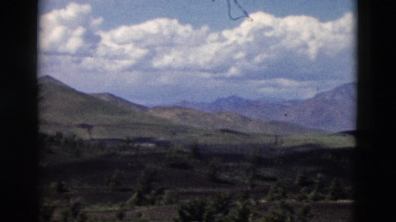 Rolling hills and distant mountains framed by dark film edges and clouds.