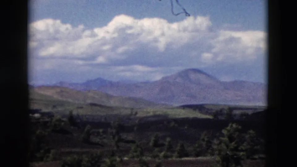 1958 Yellowstone frame showing a far ridge line, dark foreground slope, scattered trees, and a large cloud bank.