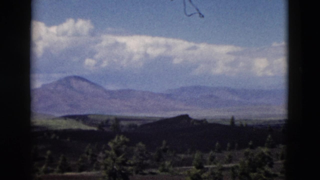 1958 Yellowstone-area 8mm view of distant mountains, low clouds, dark rolling hills, and scattered evergreen trees.