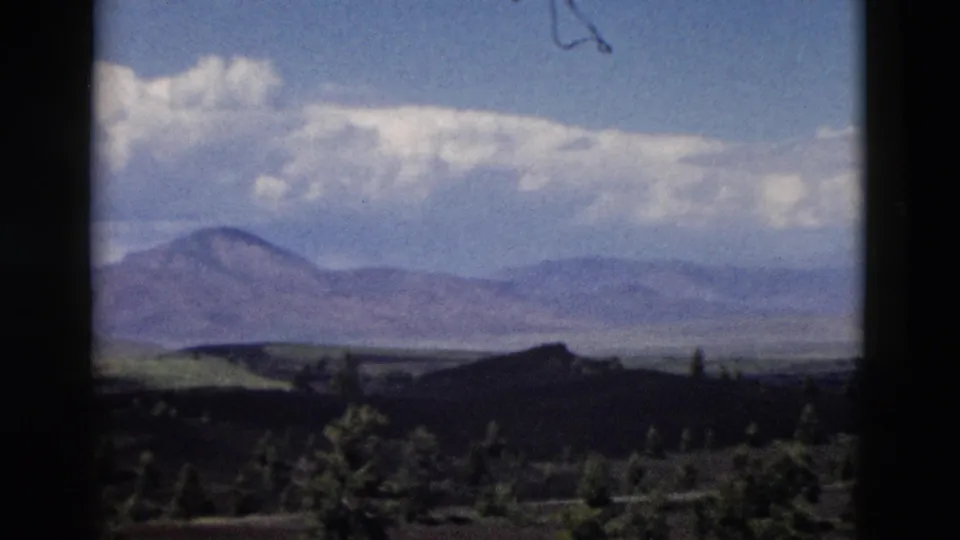 1958 Yellowstone-area 8mm view of distant mountains, low clouds, dark rolling hills, and scattered evergreen trees.