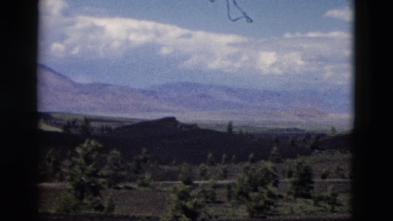 Yellowstone-area mountain landscape on 8mm film, with clouds above distant ridges and trees below.