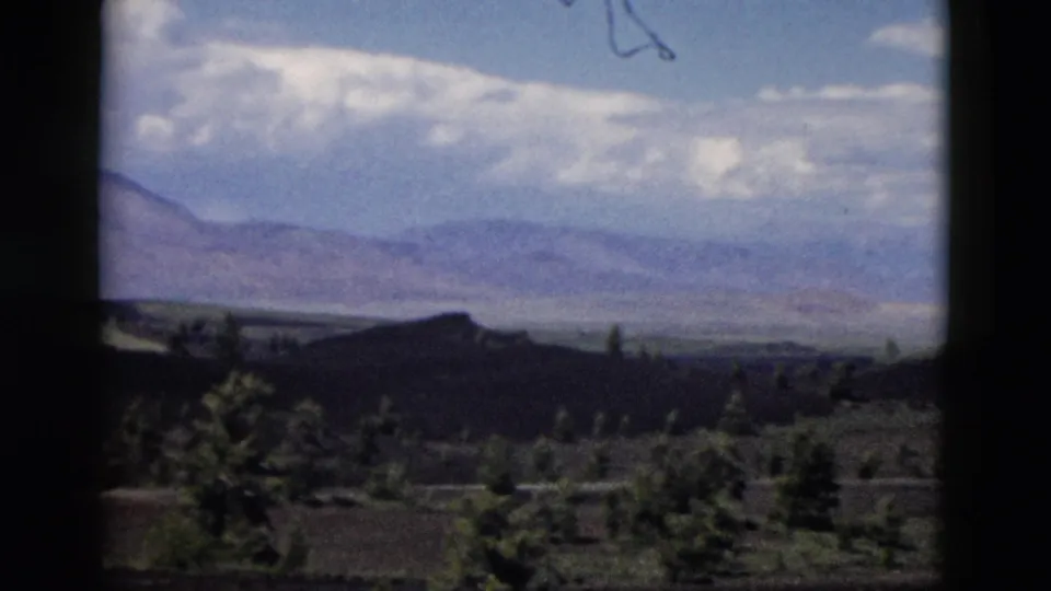 Yellowstone-area mountain landscape on 8mm film, with clouds above distant ridges and trees below.