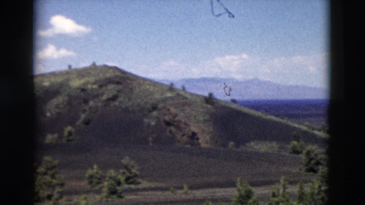 Brown hill with sparse evergreen trees under a blue sky with distant ridges.
