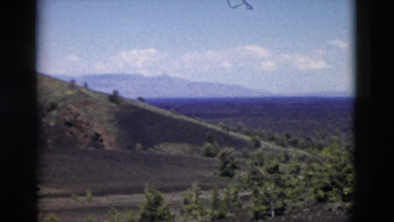 Yellowstone landscape on 8mm film, showing a sloped brown hill, green trees, and distant mountain forms.