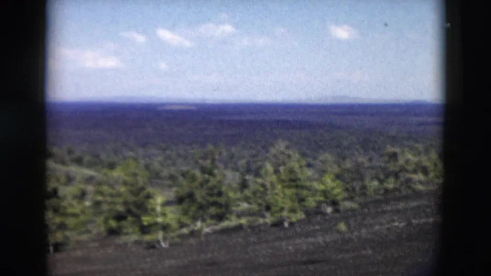 Yellowstone 8mm scenic frame showing foreground evergreens, dark volcanic-looking ground, and distant ridges.