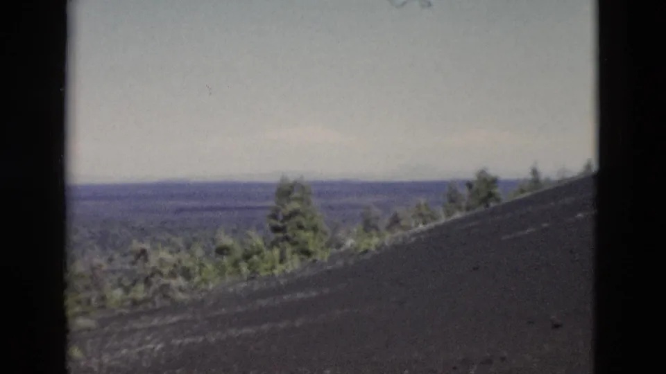 1958 Yellowstone 8mm frame showing a dark hillside, scattered trees, and hazy forest stretching into the distance.