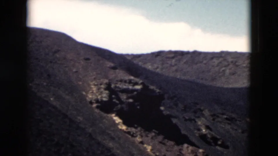 1958 Yellowstone frame showing dark volcanic terrain, an eroded crater-like depression, and a ridge under bright sky.