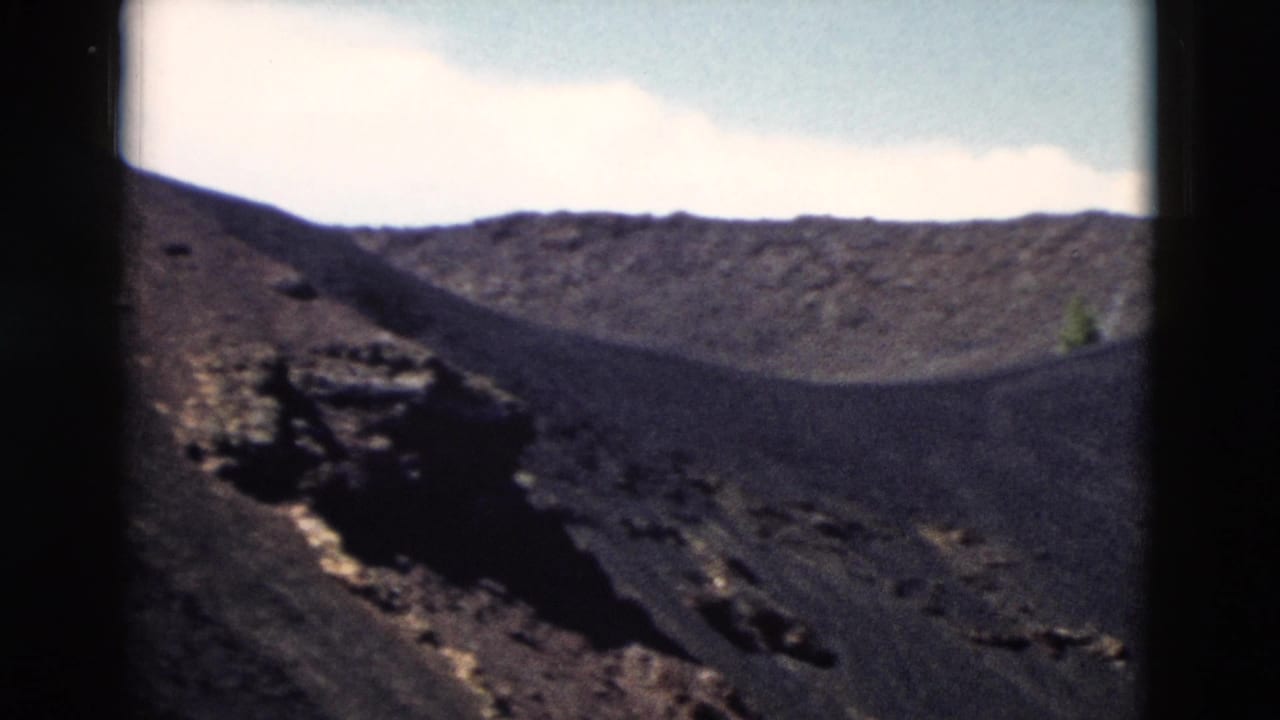 1958 Yellowstone 8mm frame showing dark volcanic slopes, rough rock, and a pale sky with clouds.