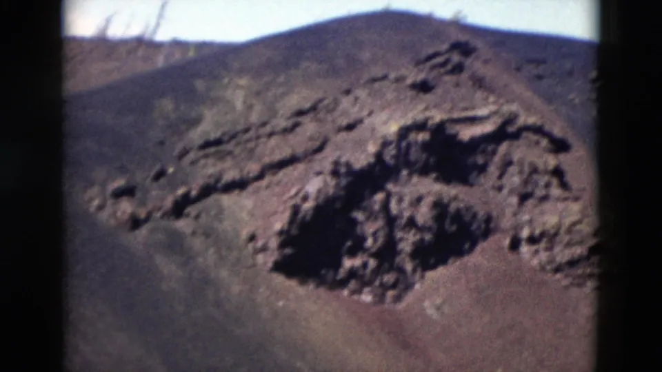 1958 Yellowstone 8mm frame centered on a rough volcanic rock outcrop with dark slopes and pale sky behind it.