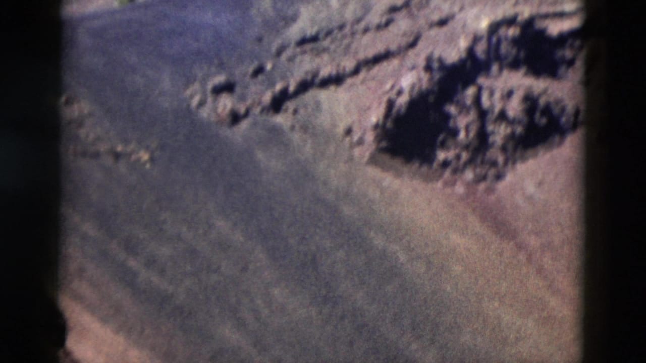 1958 8mm Yellowstone footage showing a barren brown-gray slope with a dark rocky outcrop and visible erosion channels.