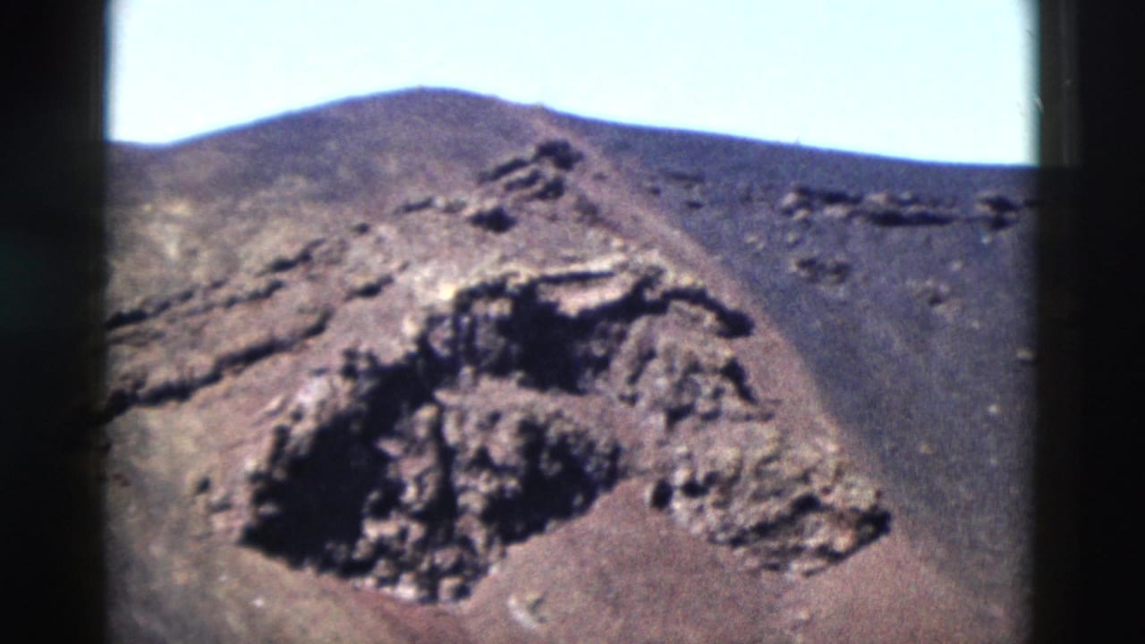 1958 Yellowstone home-movie frame with a dark rock formation on a bare mountain slope and pale sky above the ridge.