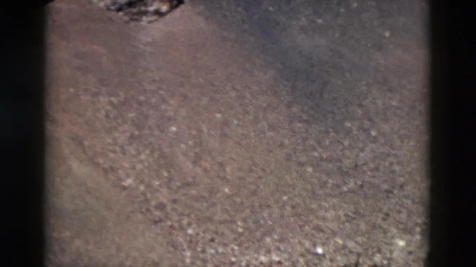 1958 Yellowstone 8mm frame showing sloped, treeless ground with scattered stones and part of a dark rocky formation near the top edge.