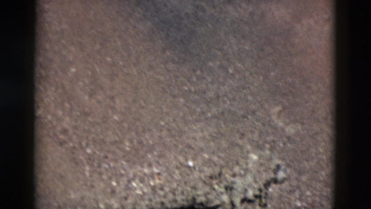 1958 Yellowstone 8mm frame showing soft, grainy close-up texture of sand, pebbles, and dark gate edges.