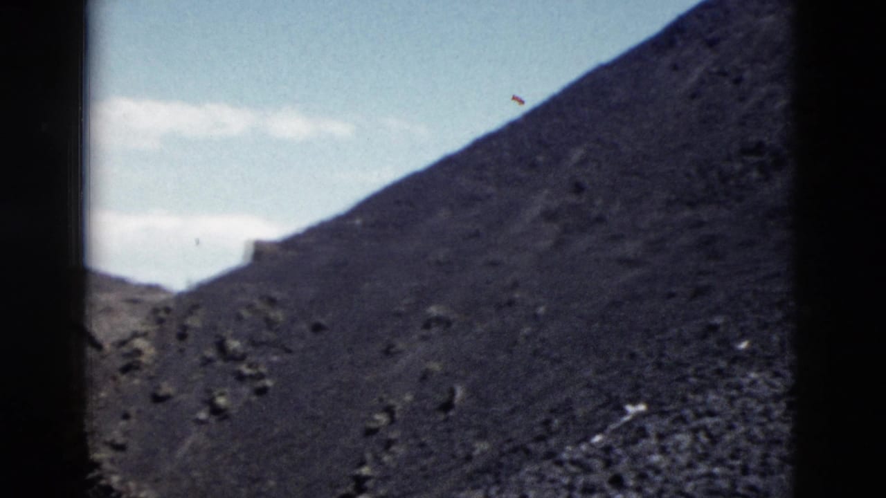1958 Yellowstone 8mm frame with a steep dark slope, scattered rocks, and pale sky above the ridge.