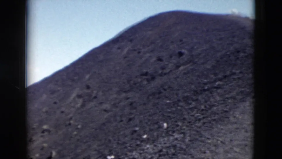 1958 Yellowstone 8mm frame showing a rounded barren slope with scattered rocks and a clear sky above.