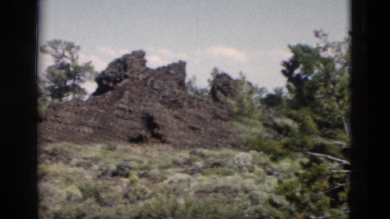 Jagged dark rock mound with trees and low vegetation around it.