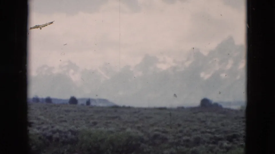1958 Yellowstone-area landscape frame showing open scrubland and a distant hazy mountain range under a pale sky.