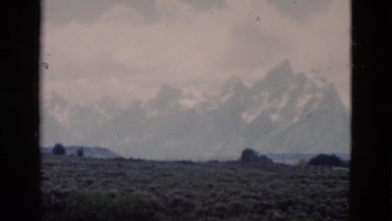 Distant snow-capped mountains beyond a scrub plain under a cloudy sky.