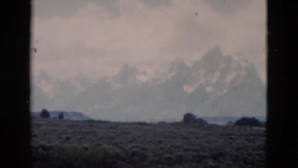 1958 Wyoming 8mm frame showing distant snow-capped mountains, open scrub plain, cloudy sky, and dark film borders.