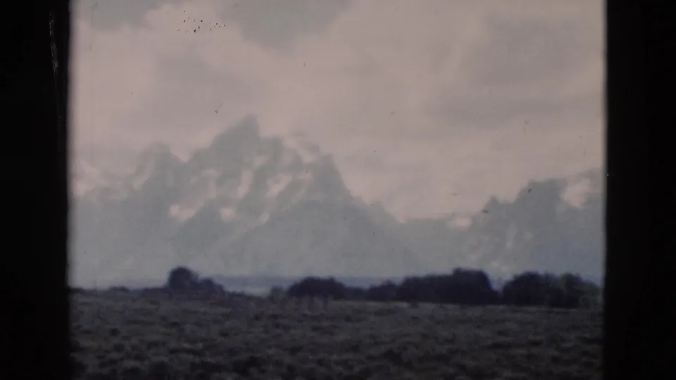 1958 Wyoming 8mm still showing rugged snow-dusted peaks, dark low trees, open ground, and soft home-movie focus.