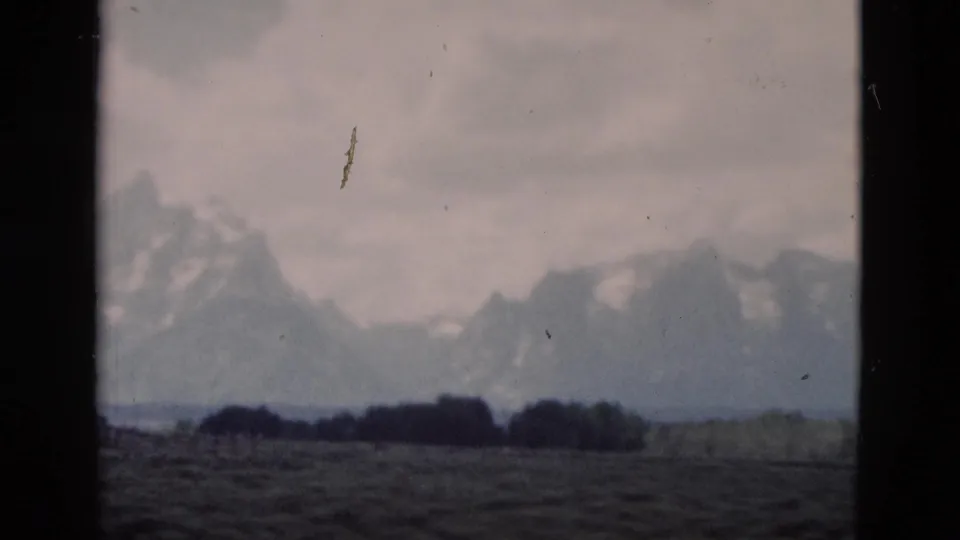End frame from a 1958 Yellowstone-area 8mm pan, with distant mountains, flat scrubland, low trees, clouds, and film wear.